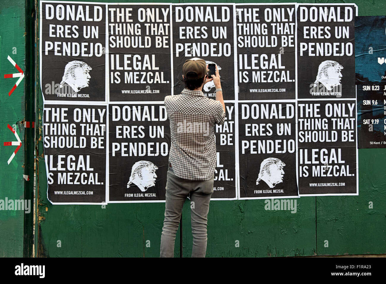 A man takes photos of posters on Bedford Ave in Brooklyn calling Donald Trump a pendejo which is Spanish for idiot & mocking his immigration policy. Stock Photo