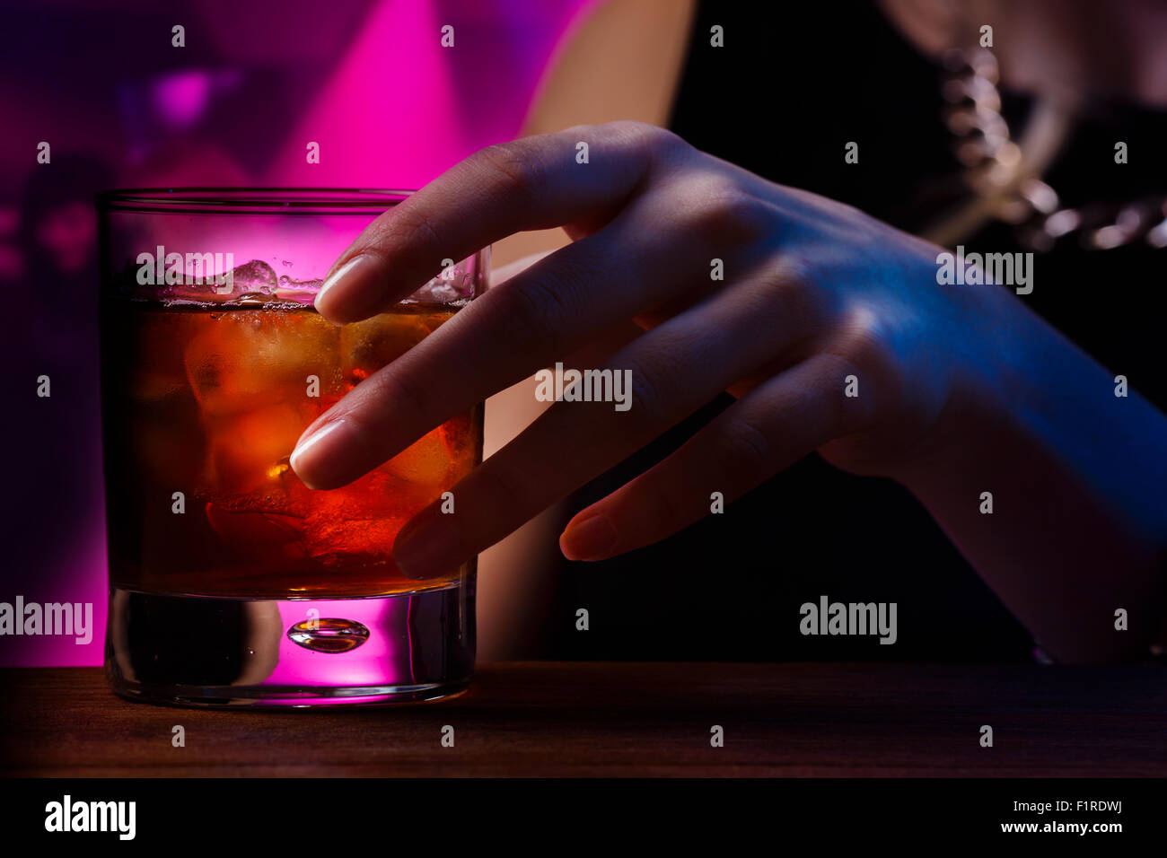 Woman's hand holding old fashioned glass with cold cocktail against blurred night club background Stock Photo