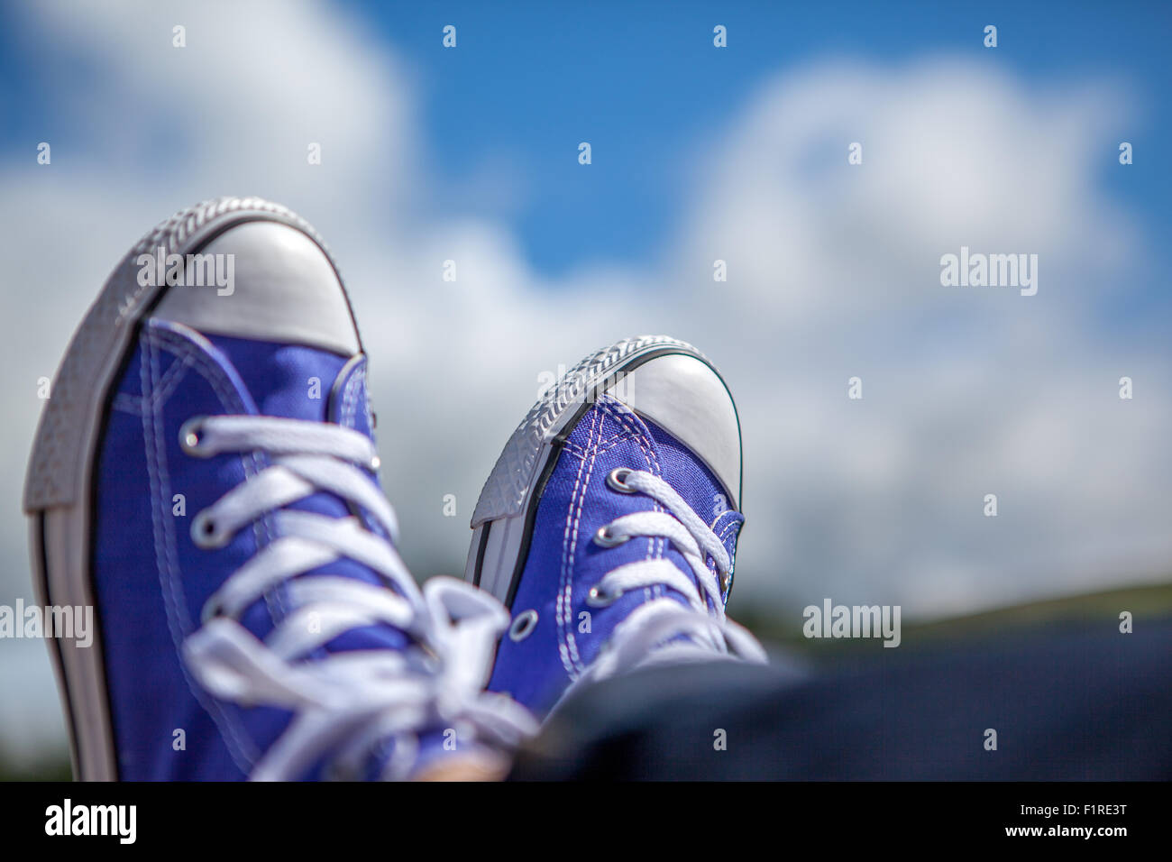 White laced blue high top trainers against a blue sky and white clouds Stock Photo