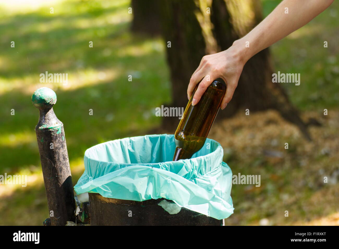 Hand of woman throwing glass bottle into old trash can, concept of
