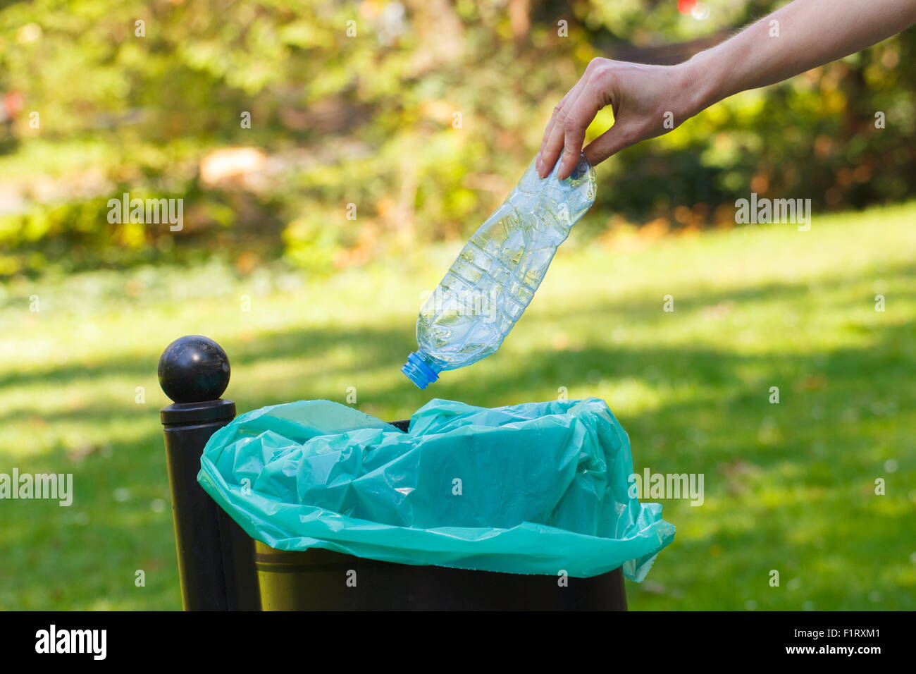 Hand of woman throwing plastic bottle into old trash can, concept of