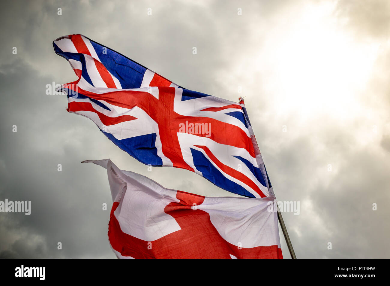 English Union Jack and saint George flag flying in the wind against a grey cloudy sky Stock Photo