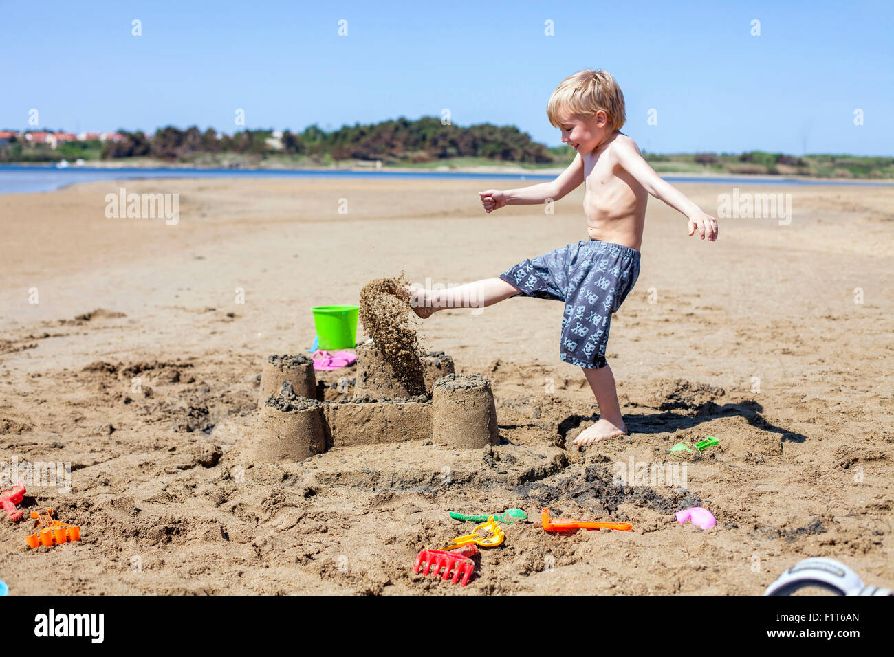 Boy kicking against sandcastle on beach Stock Photo