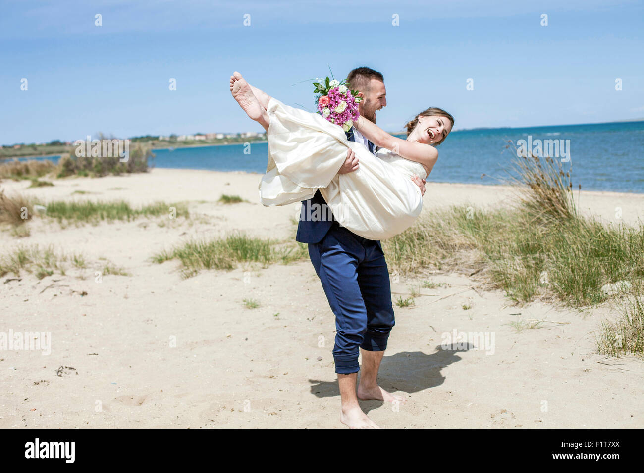 Bridegroom carrying bride on beach Stock Photo