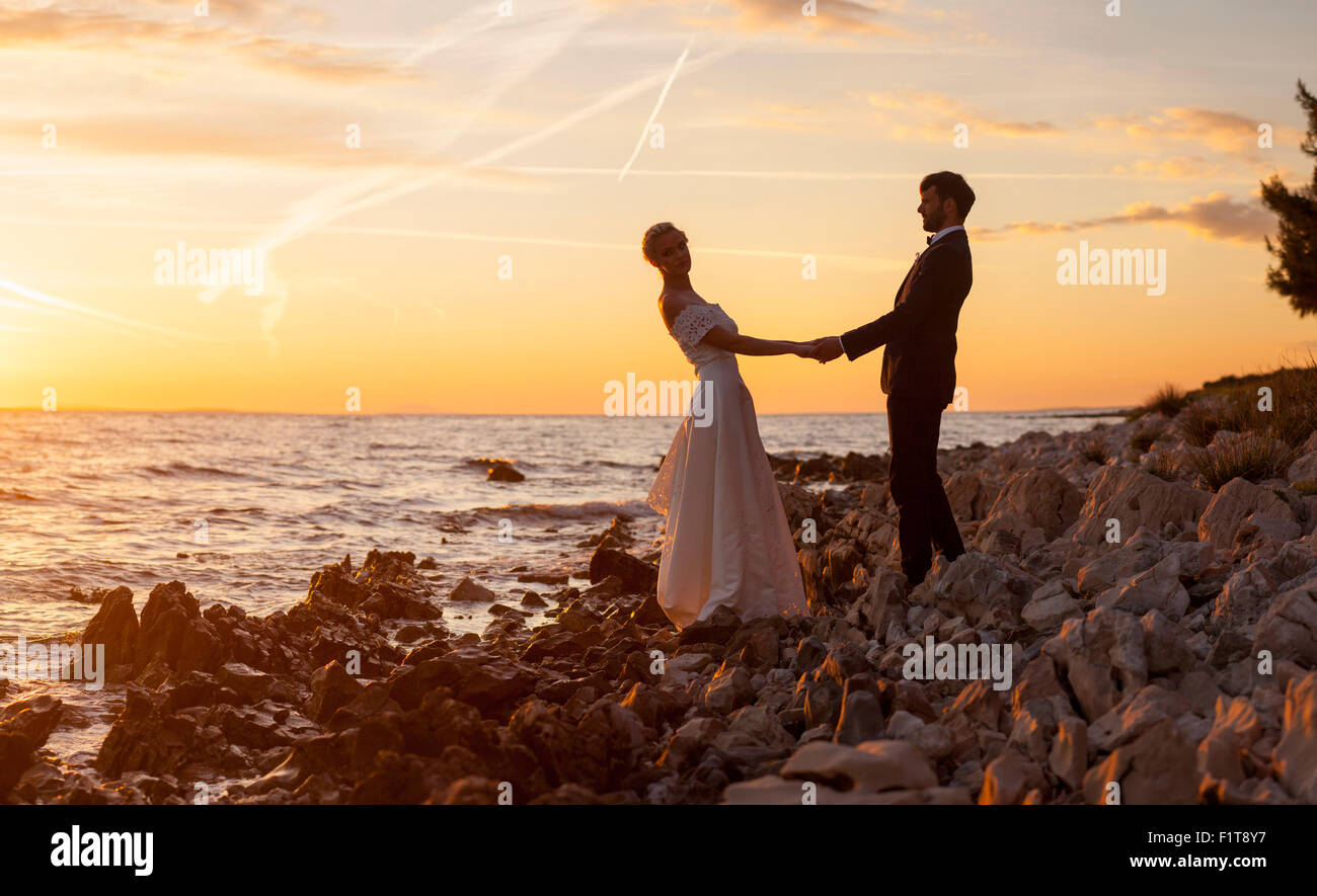 Bride and groom holding hands against sunset Stock Photo