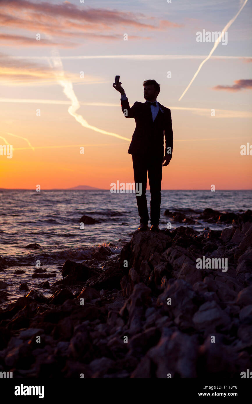 Groom taking picture of himself against sunset Stock Photo