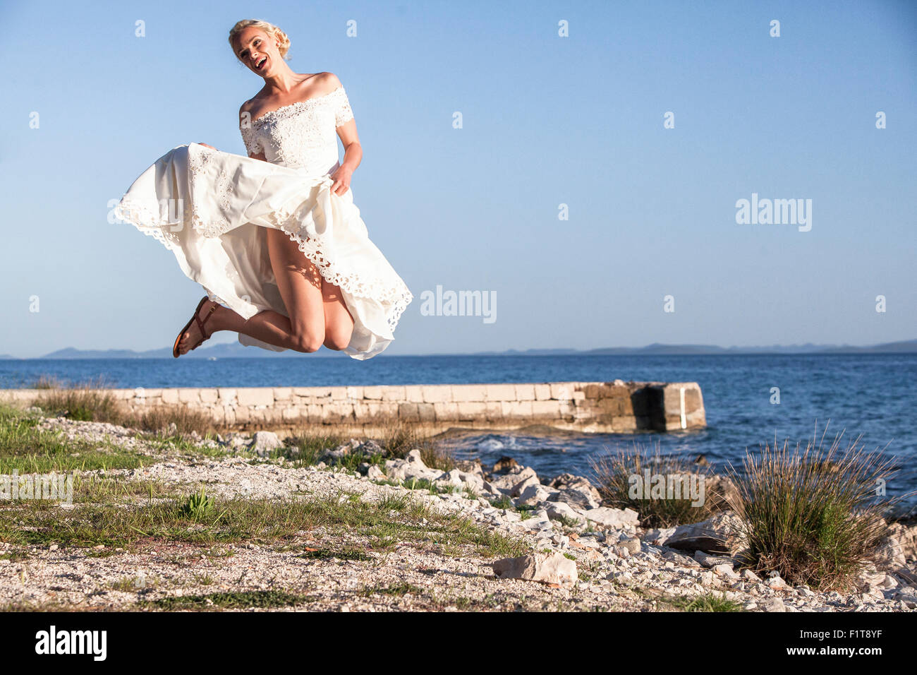Bride in wedding dress jumping against blue sky Stock Photo