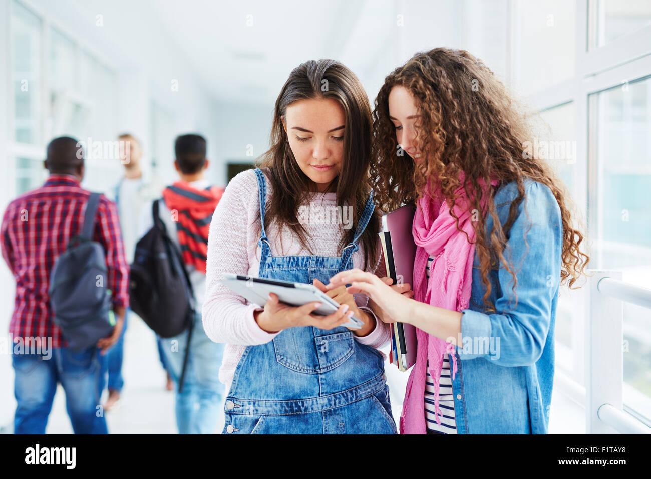 Modern teenage girls with touchpad networking in college corridor Stock
