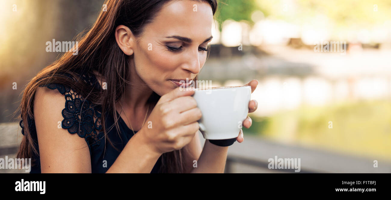 Close up portrait of young woman with an aromatic coffee in hands. Female drinking coffee at cafe. Stock Photo