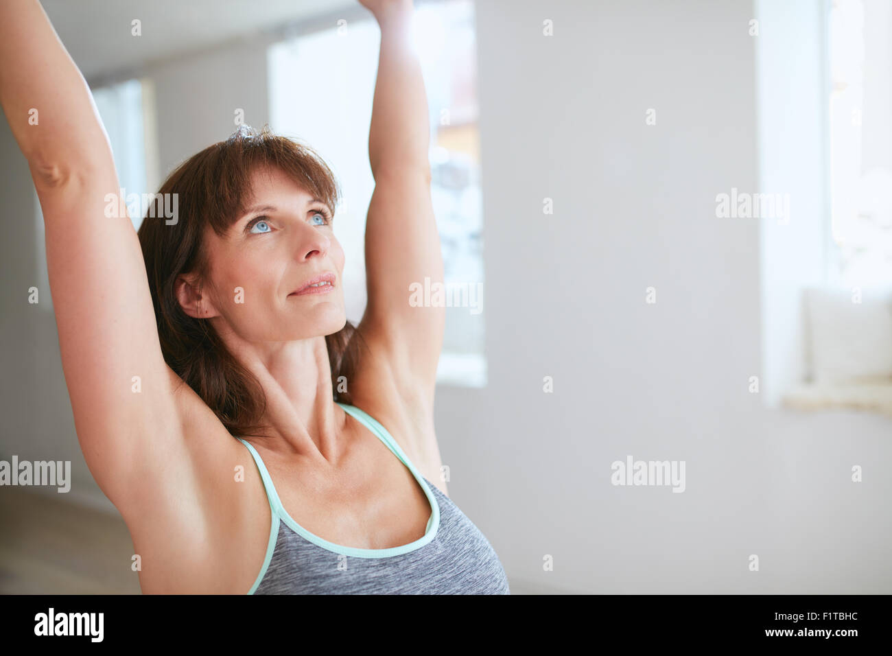 Close up shot of mature woman practicing yoga with her arms raised and looking upwards at gym. Fitness female in warrior pose I Stock Photo