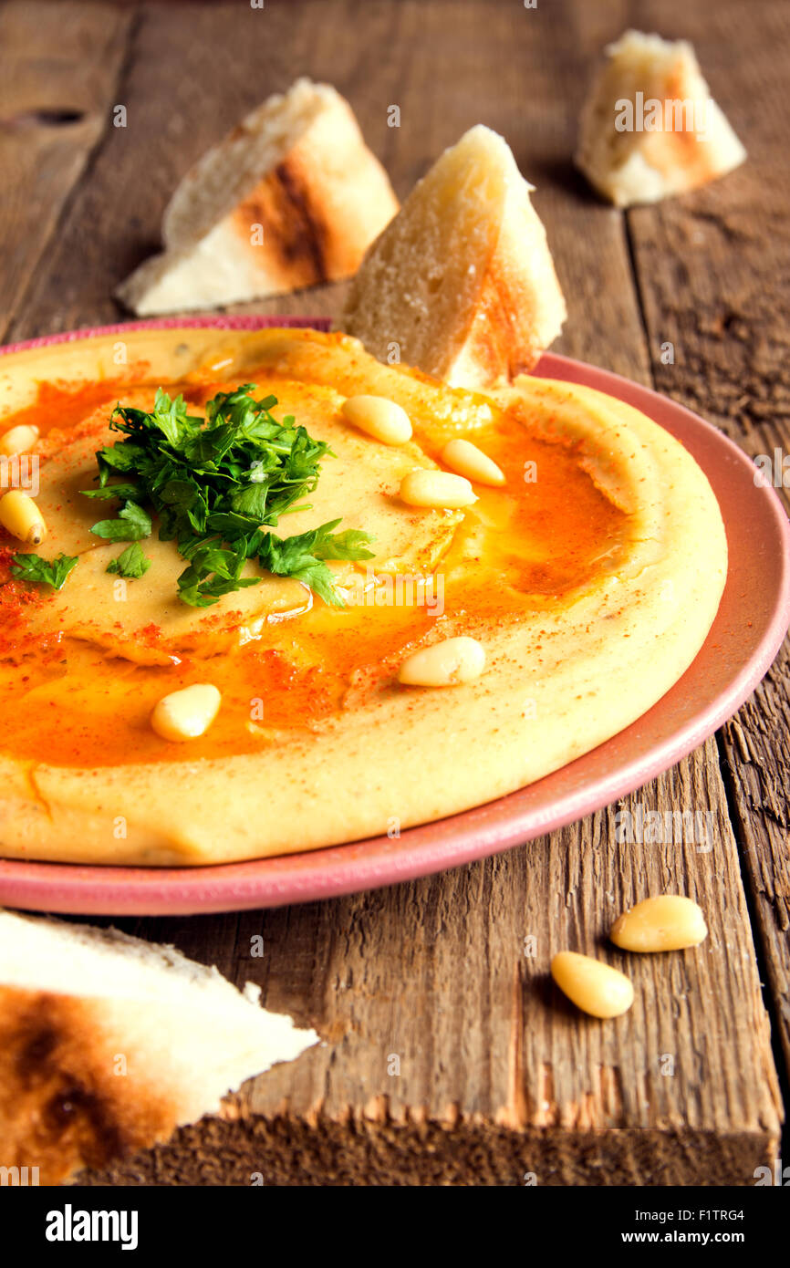 Hummus with parsley, pine nuts on plate and rustic wooden background close up Stock Photo