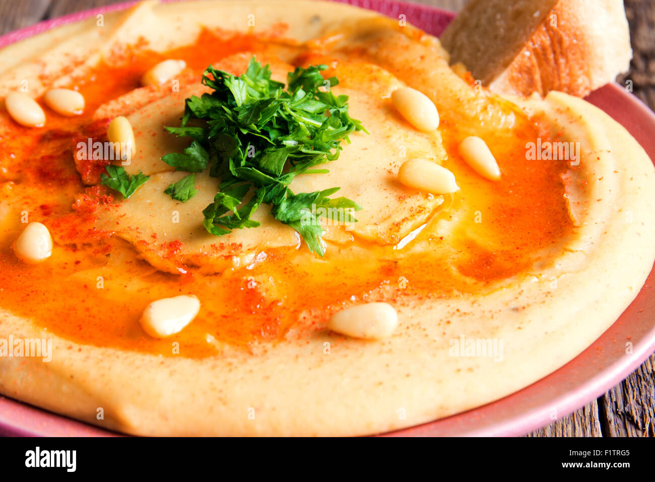 Hummus with parsley, pine nuts on plate and rustic wooden background close up Stock Photo