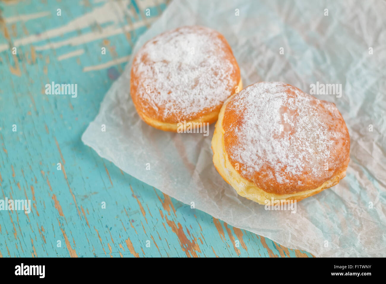 Sweet sugary donuts on rustic wooden kitchen table, tasty bakery doughnuts on crumpled baking paper in vintage retro toned image Stock Photo