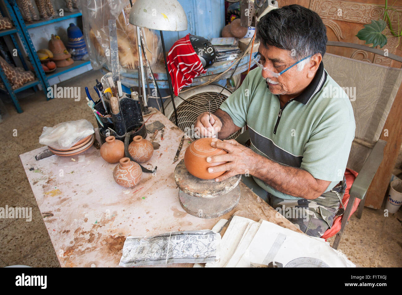 Señor Mena decorates pottery via etching. An artisan etches pottery using old Mayan patterns.  A photocopy of one lies in front Stock Photo