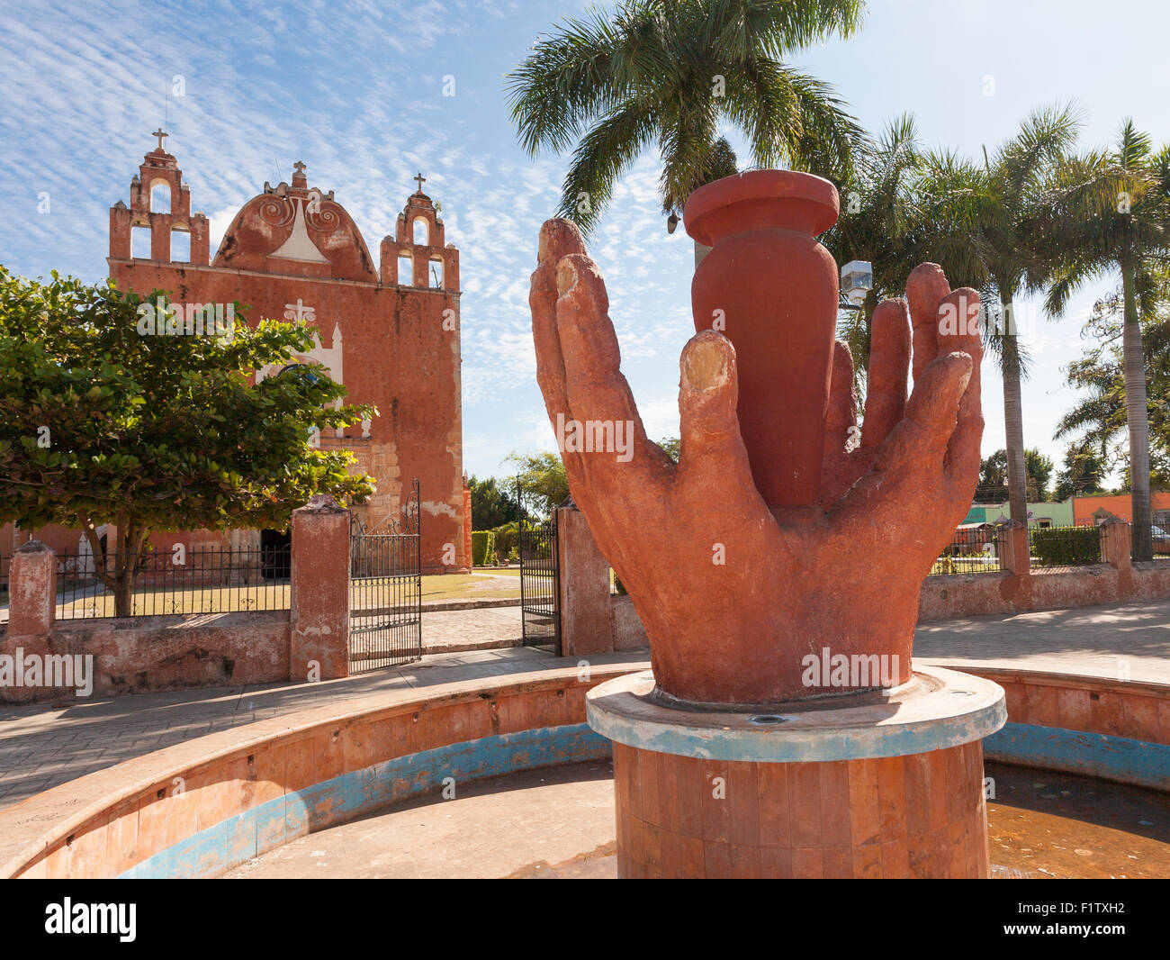 Hands of the potter in red clay frame a view of Ticul's main church. The red hands echo the