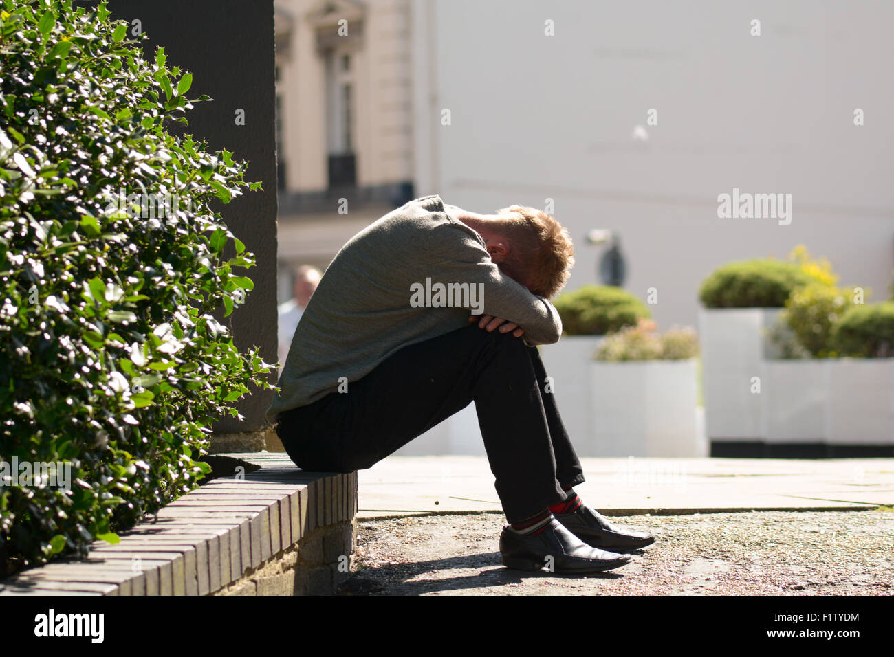 Man sat on low wall with his head buried in his hands in Bedford