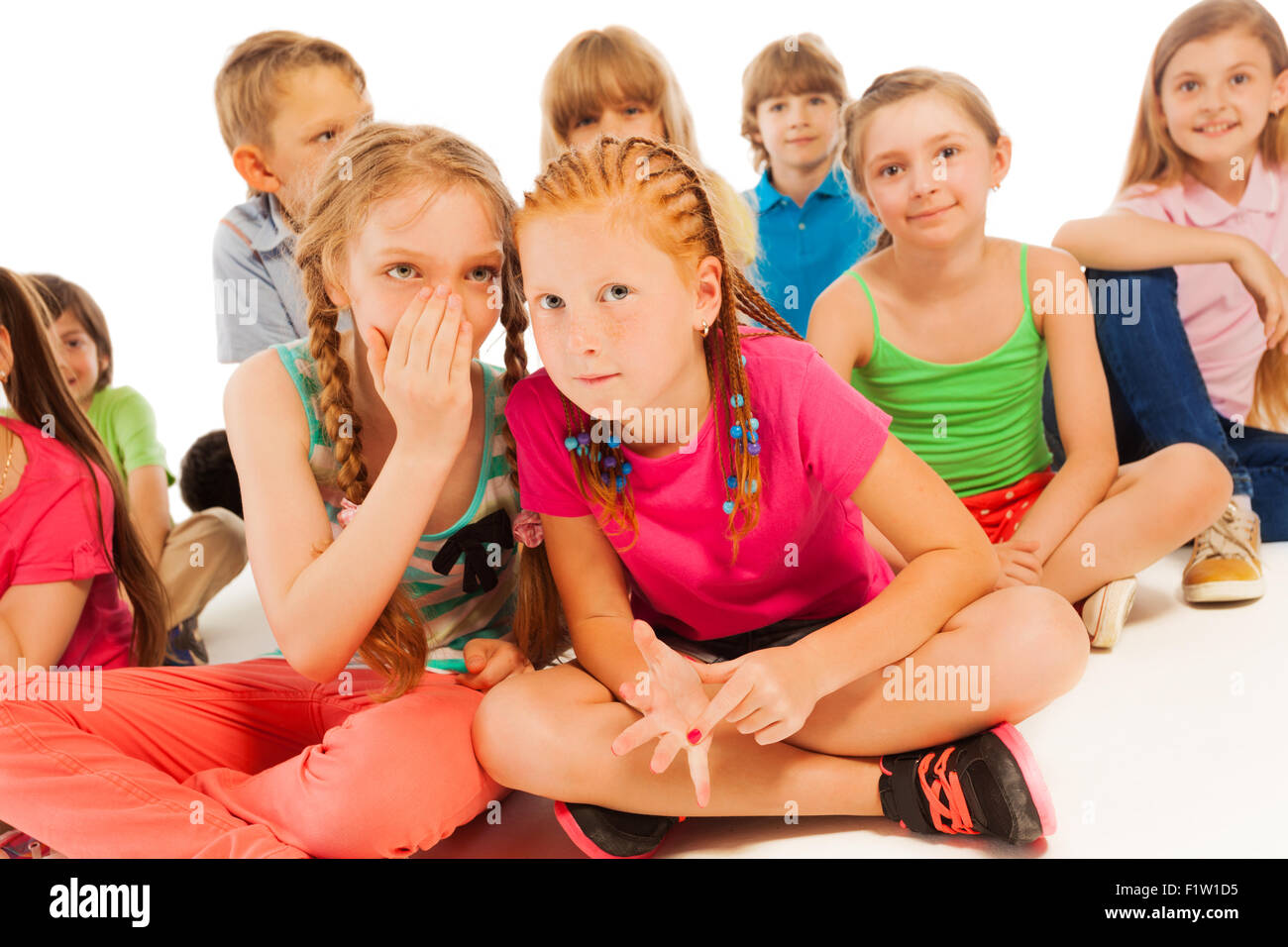Two whispering girls sit among other friends Stock Photo