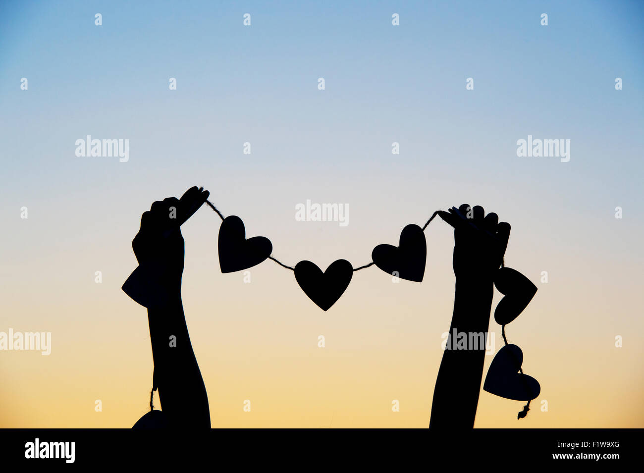 Girls hands holding hearts on a string at sunset. Silhouette Stock Photo