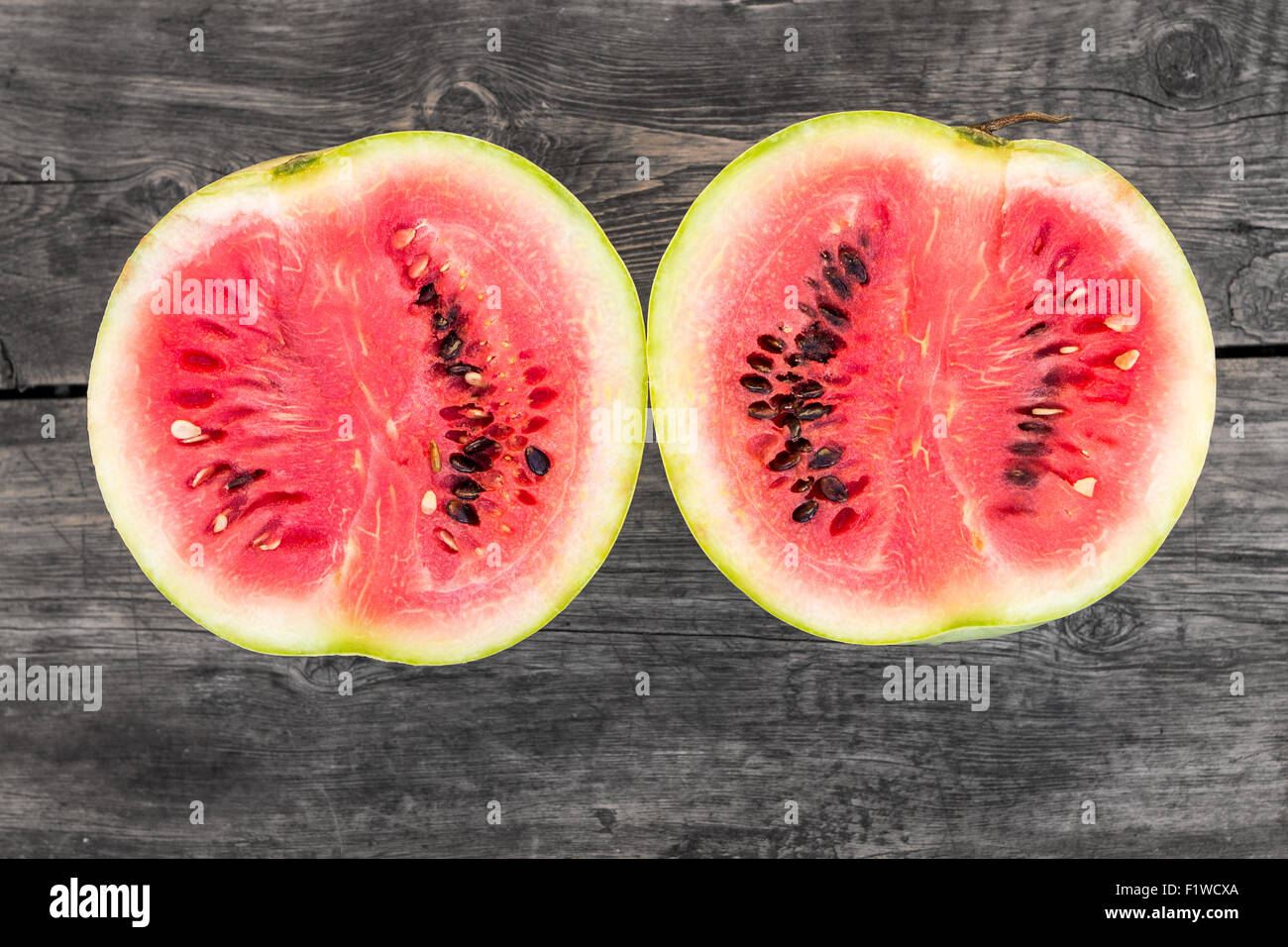 Two pieces of cut in half ripe fresh watermelon on wooden background. Top view image Stock Photo