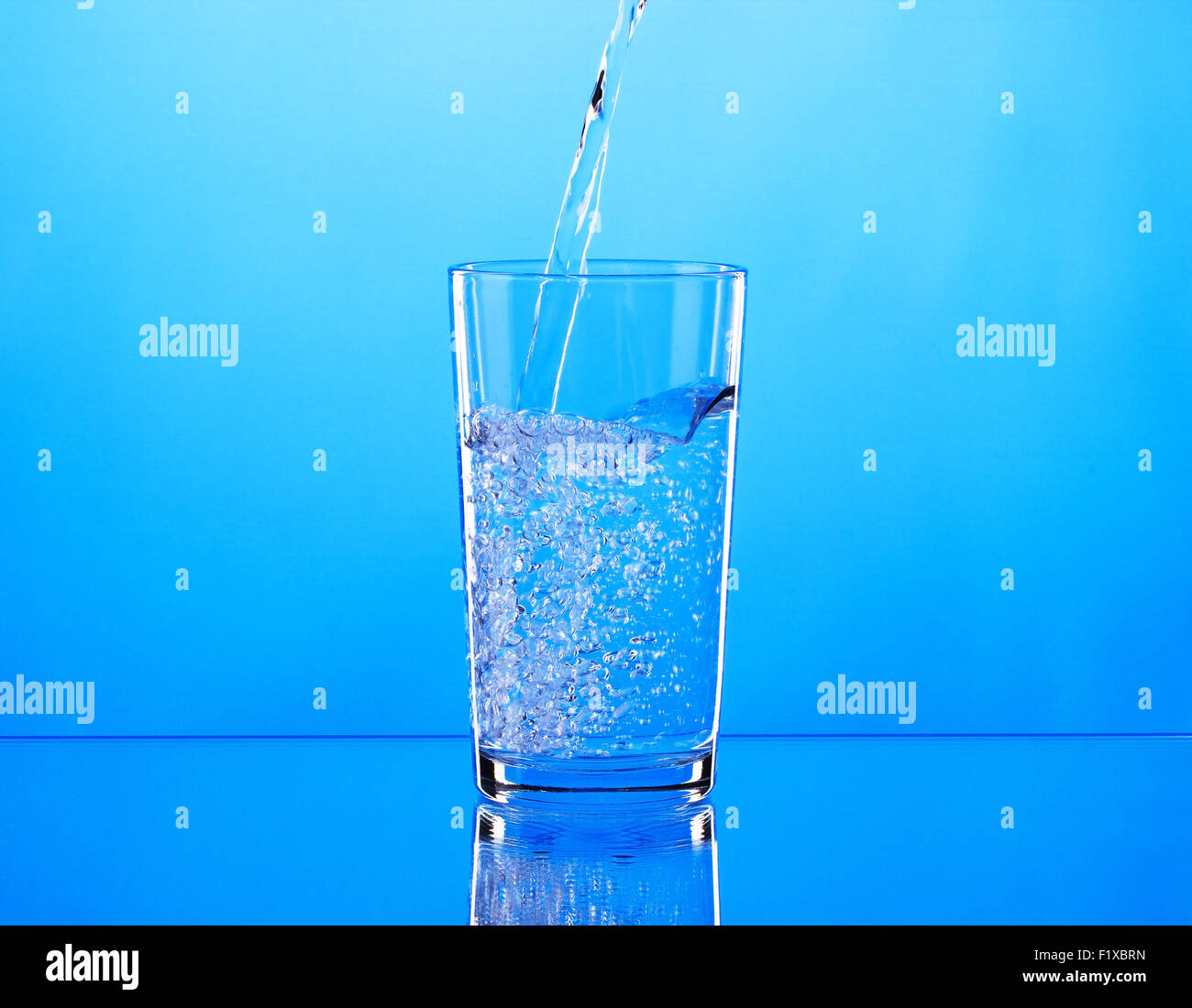 Pouring water into glass on blue background. Stock Photo