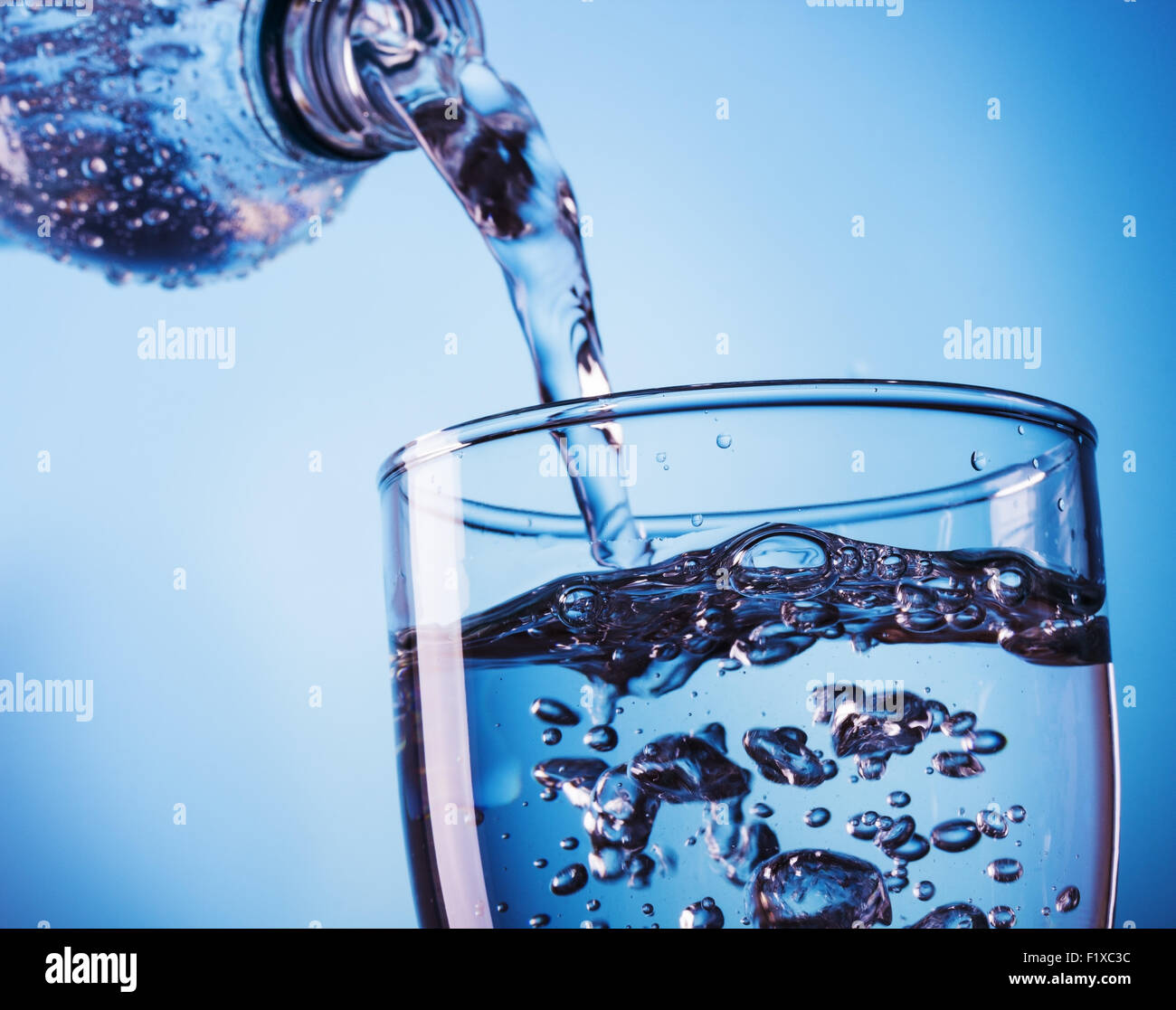 Pouring water from bottle into glass on blue background Stock Photo