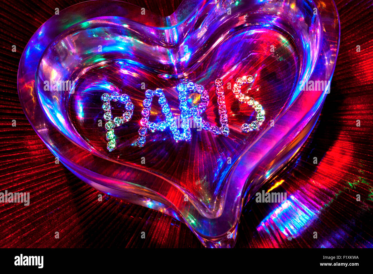 Sparkling jewel PARIS motif on heart shaped crystal glass with multicolored lighting in romantic evening situation Stock Photo