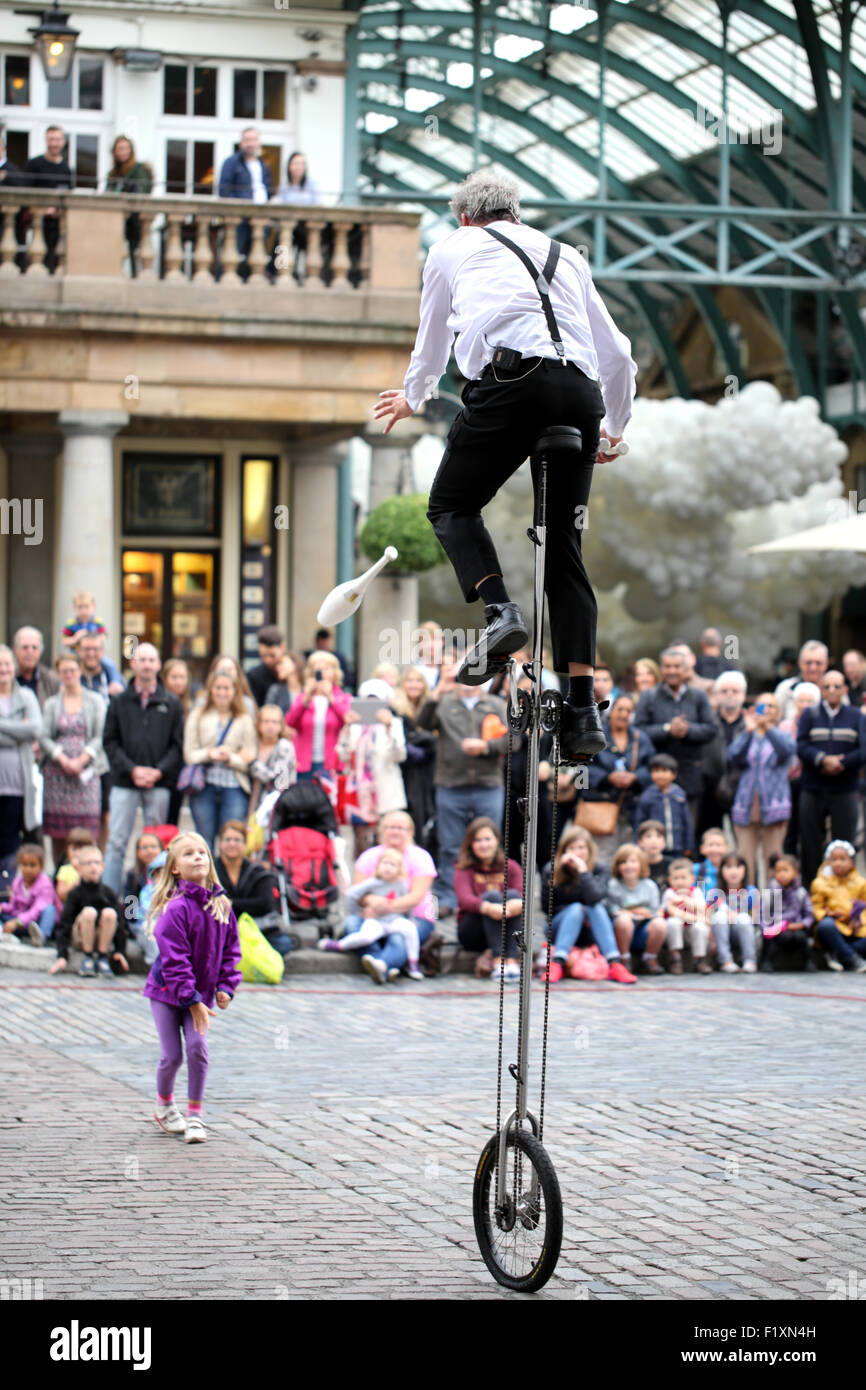 A street entertainer using a young girl as a stooge riding a uni cycle and entertaining a large crowd in Covent garden, London Stock Photo