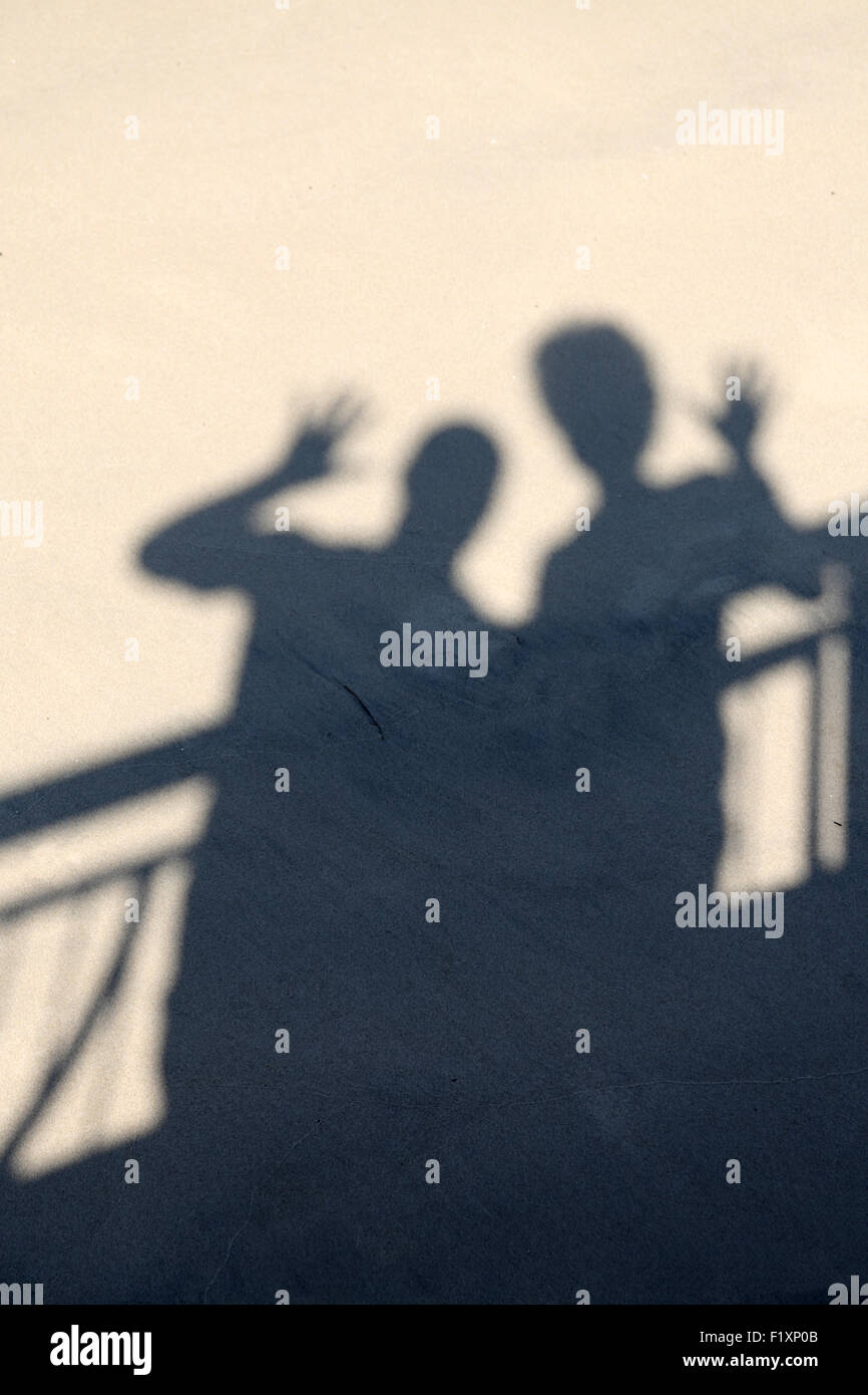 Clear crisp shadows of two people waving falling from a balcony onto a beach. It's a simple fun image Stock Photo