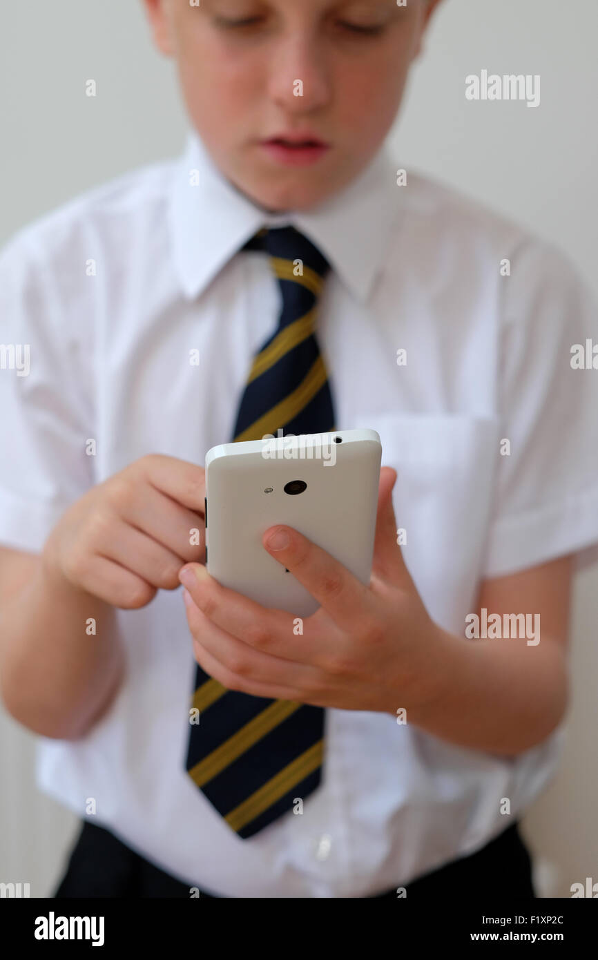 A school child in uniform using his mobile phone ( texting ) UK Stock Photo