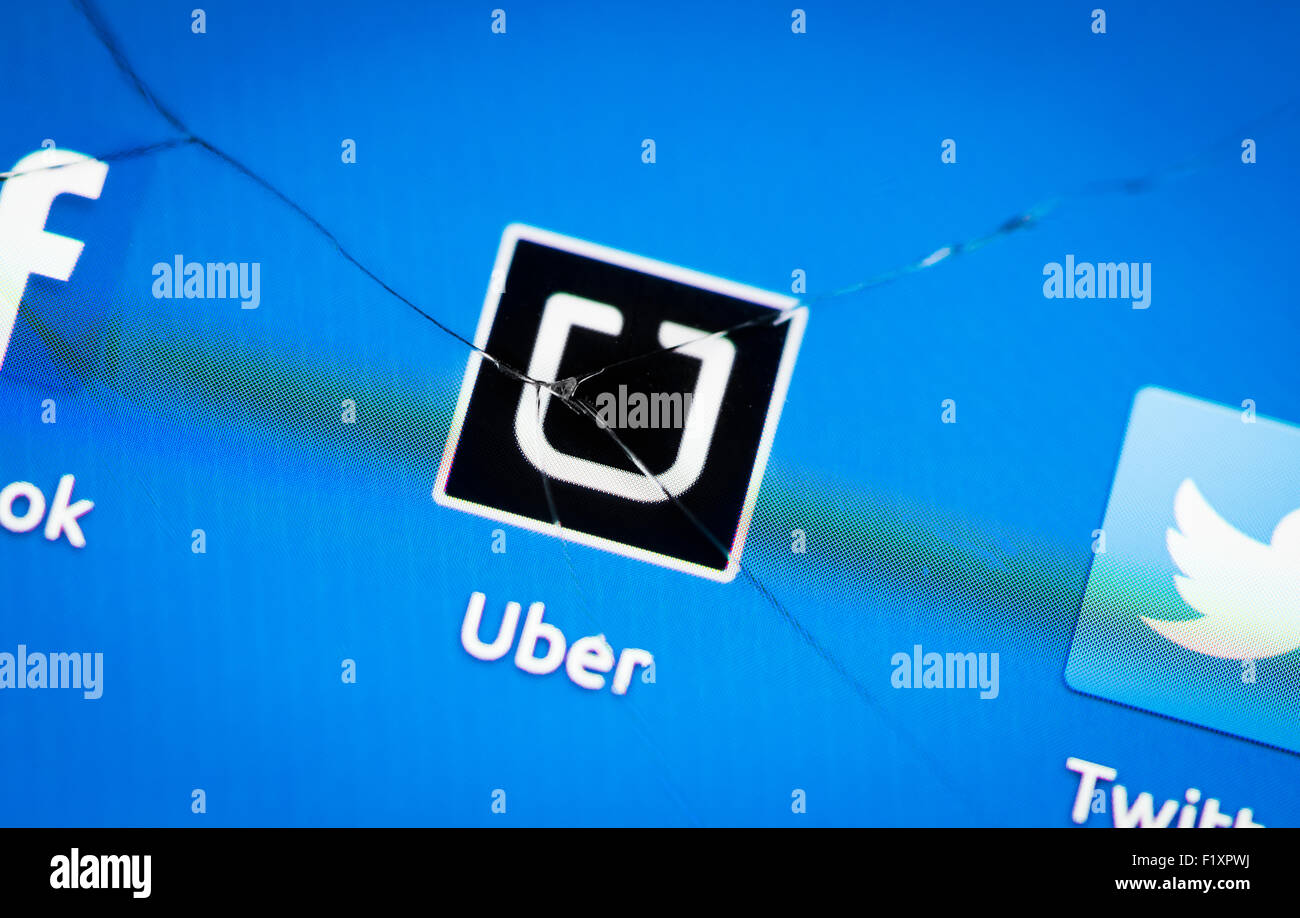 The icon of the Uber taxi service app is displayed on a smartphone behind a large crack in the touchscreen's glass. Stock Photo