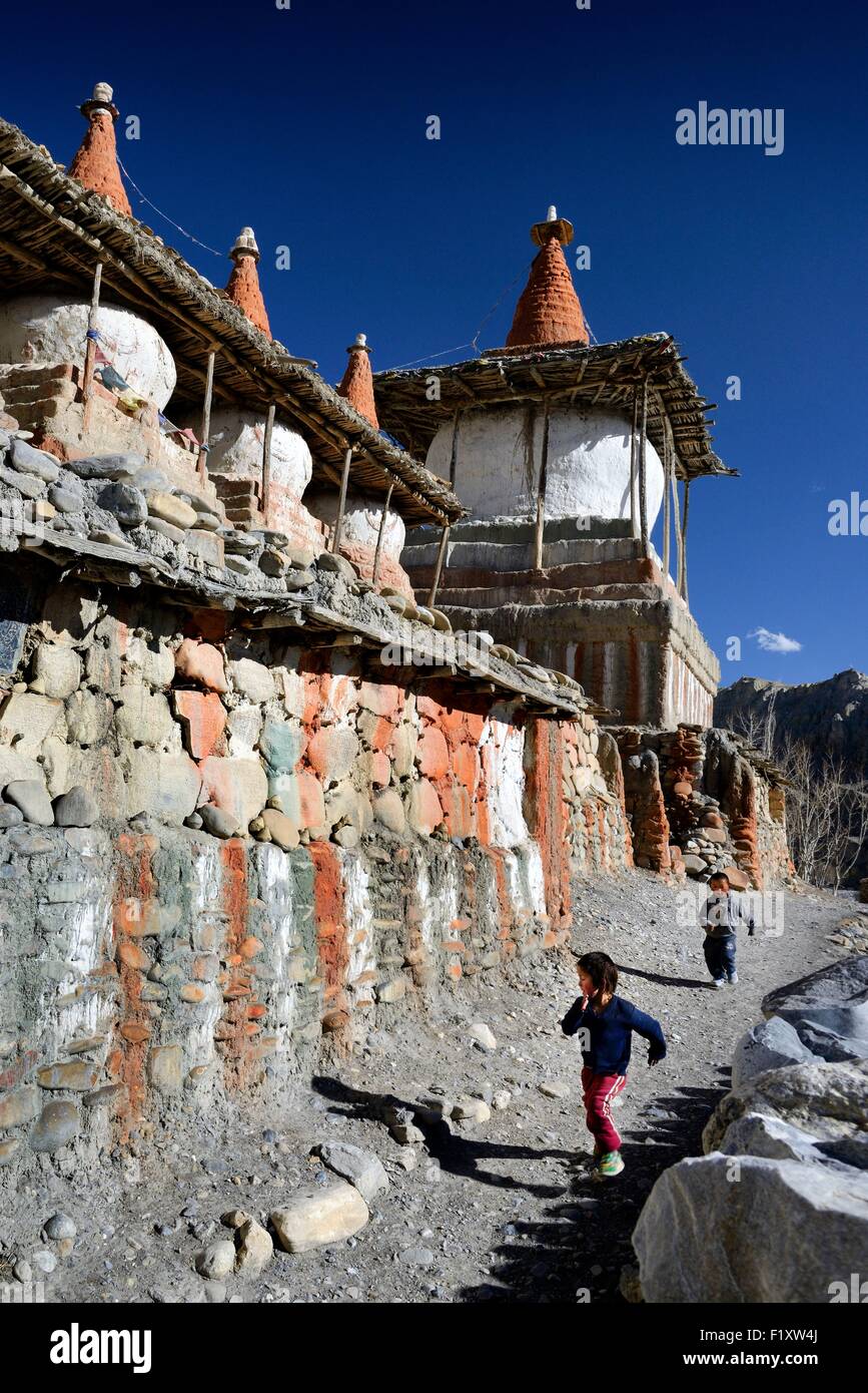 Nepal, Gandaki zone, Upper Mustang (near the border with Tibet), boys running along a mani wall (stones inscribed with a buddhist mantra) and stupa (chorten) in the village of Tangge Stock Photo
