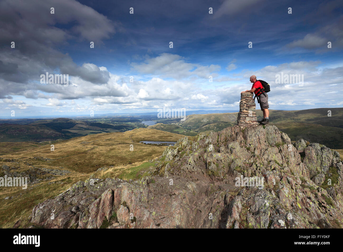 Walker at the Summit cairn and OS Trig Point on Place Fell, Lake District National Park, Cumbria, England, UK. Stock Photo