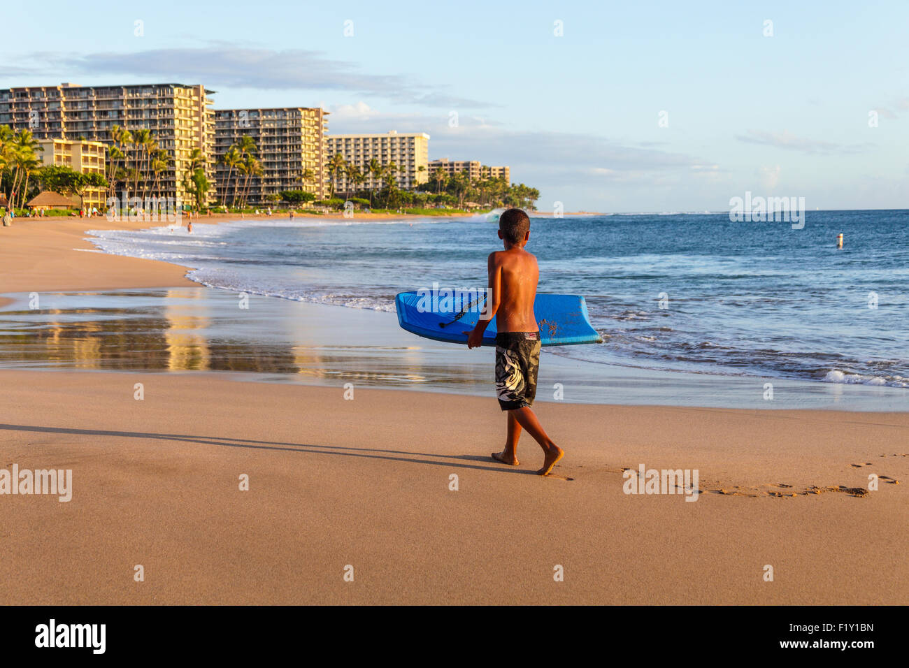 Boy with skim board eyes sea at Kaanapali Beach on Maui at sunset Stock Photo