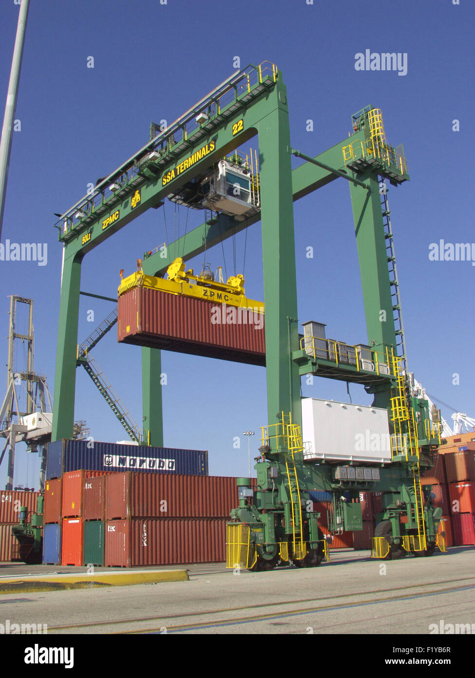 shipping container being handled by a transtainer crane at port