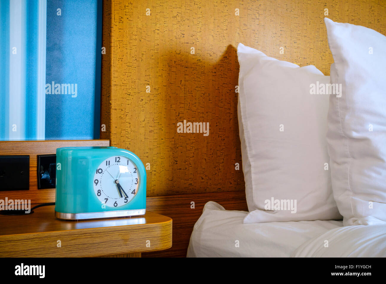Fragment of a bed and a bedside table with alarm clock at a hotel Stock Photo