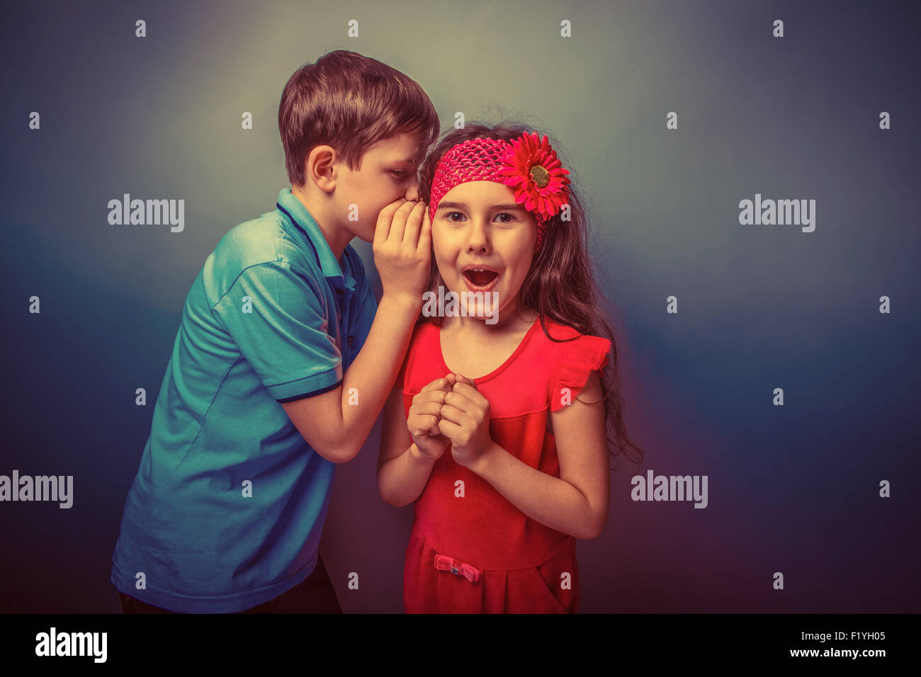 Teen boy whispering in the ear of teen girl on  a gray  backgrou Stock Photo