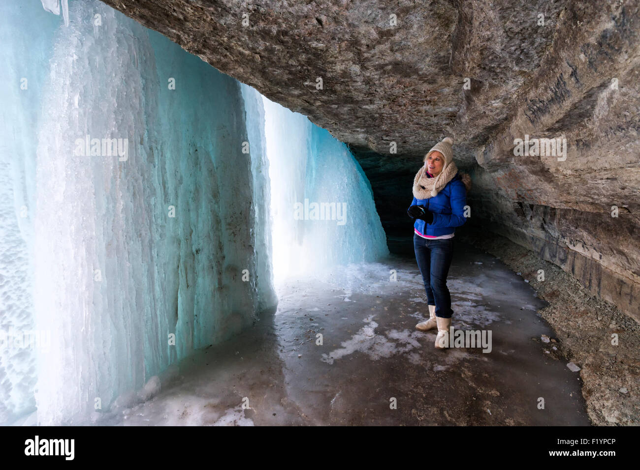Caucasian woman in winter clothing explores behind frozen Minnehaha Falls in winter, Minneapolis, MN, USA Stock Photo