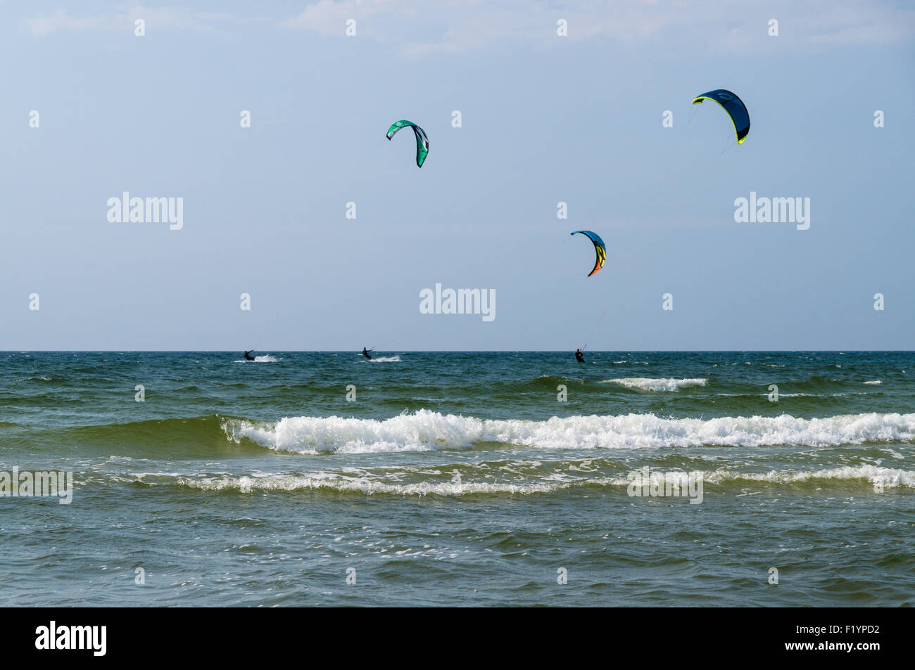 Silhouettes of three kiters ride on the waves of sea Stock Photo