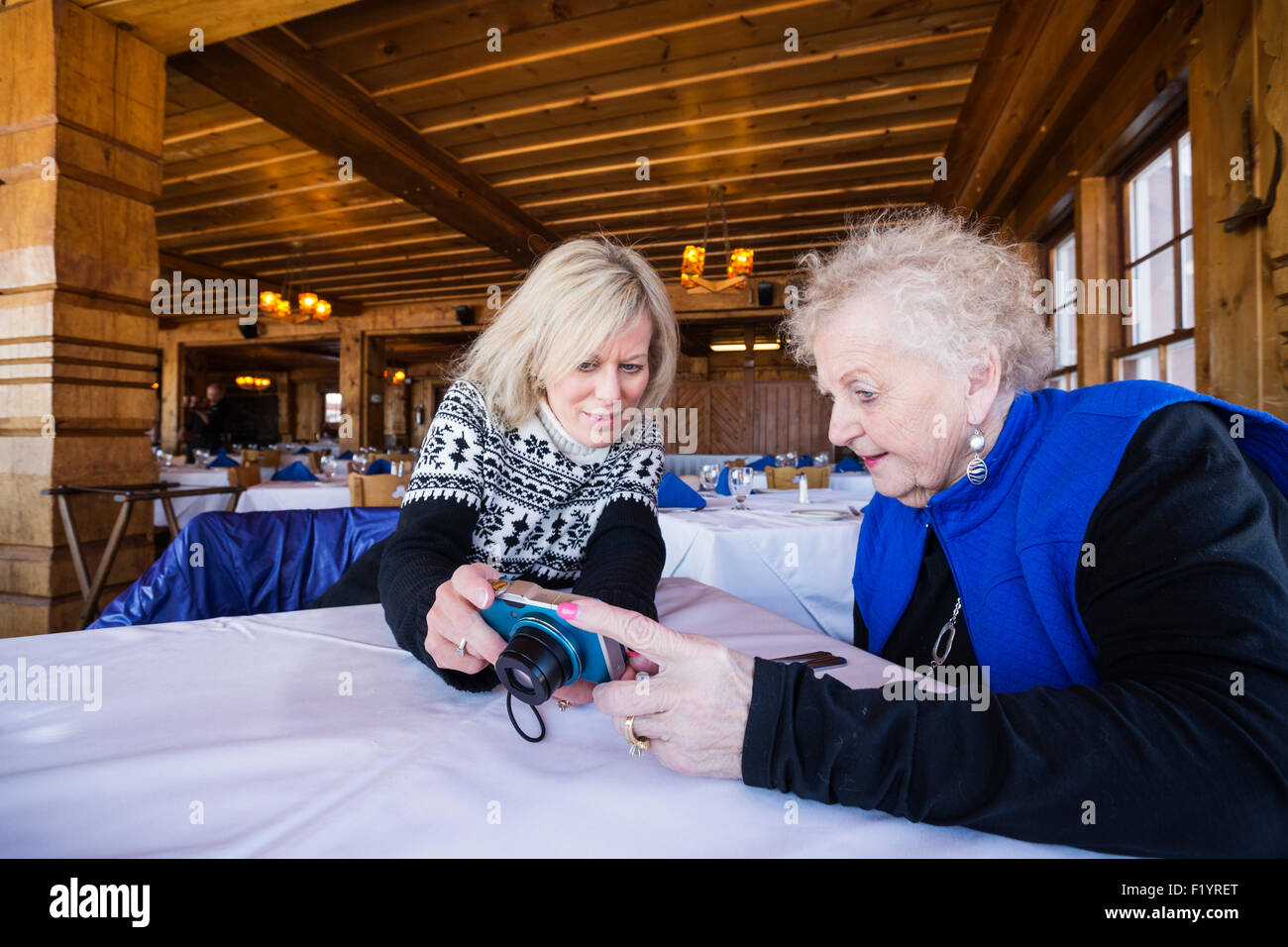 Senior mother and adult daughter look at back of digital camera while waiting for lunch inside a log dining room, Lutsen, MN Stock Photo