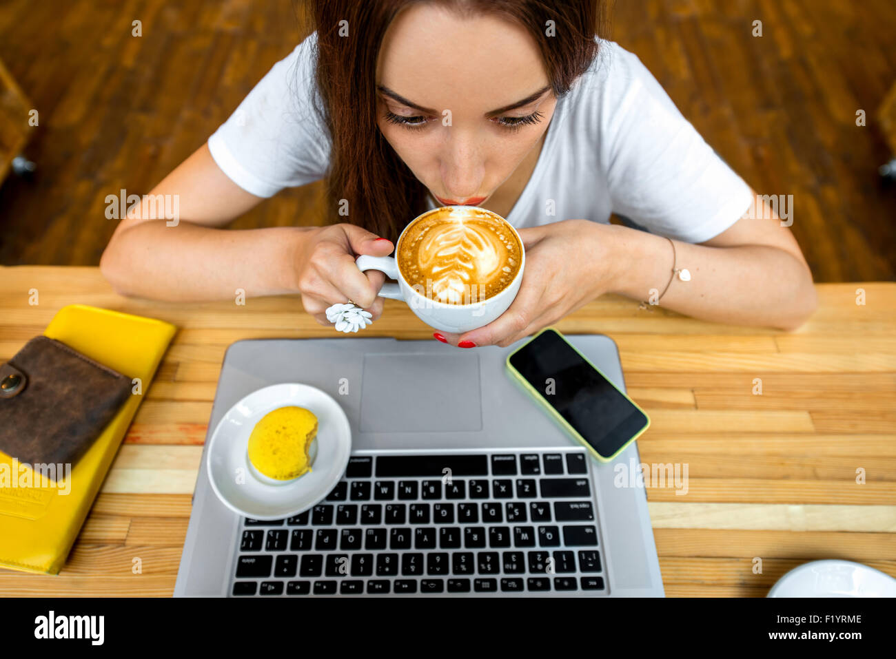 Woman enjoying cappuccino sitting with laptop Stock Photo