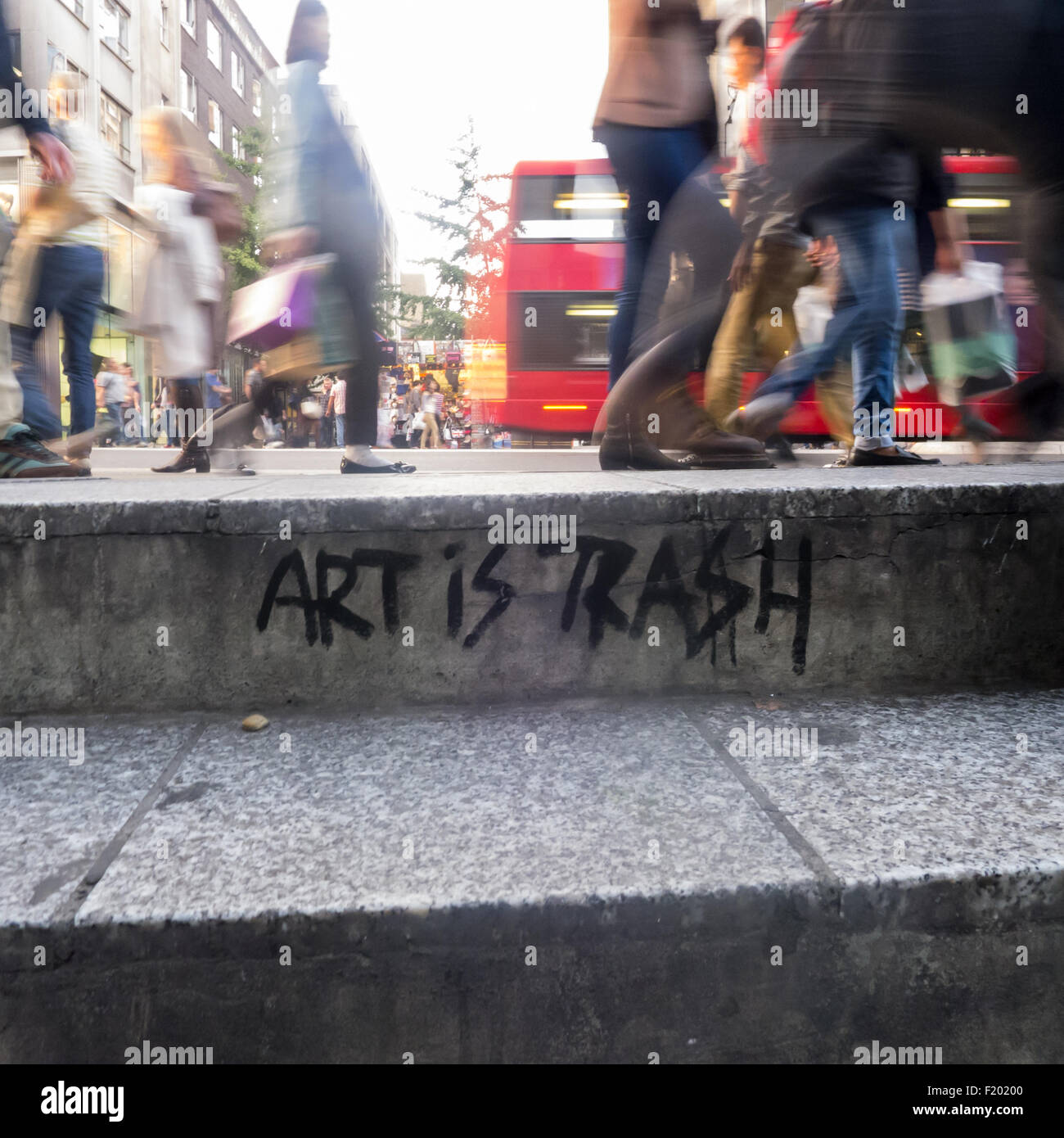London, England. Street kerb with 'Art is Trash' graffiti, with pedestrian feet, in blue trainers and polished leather. Stock Photo