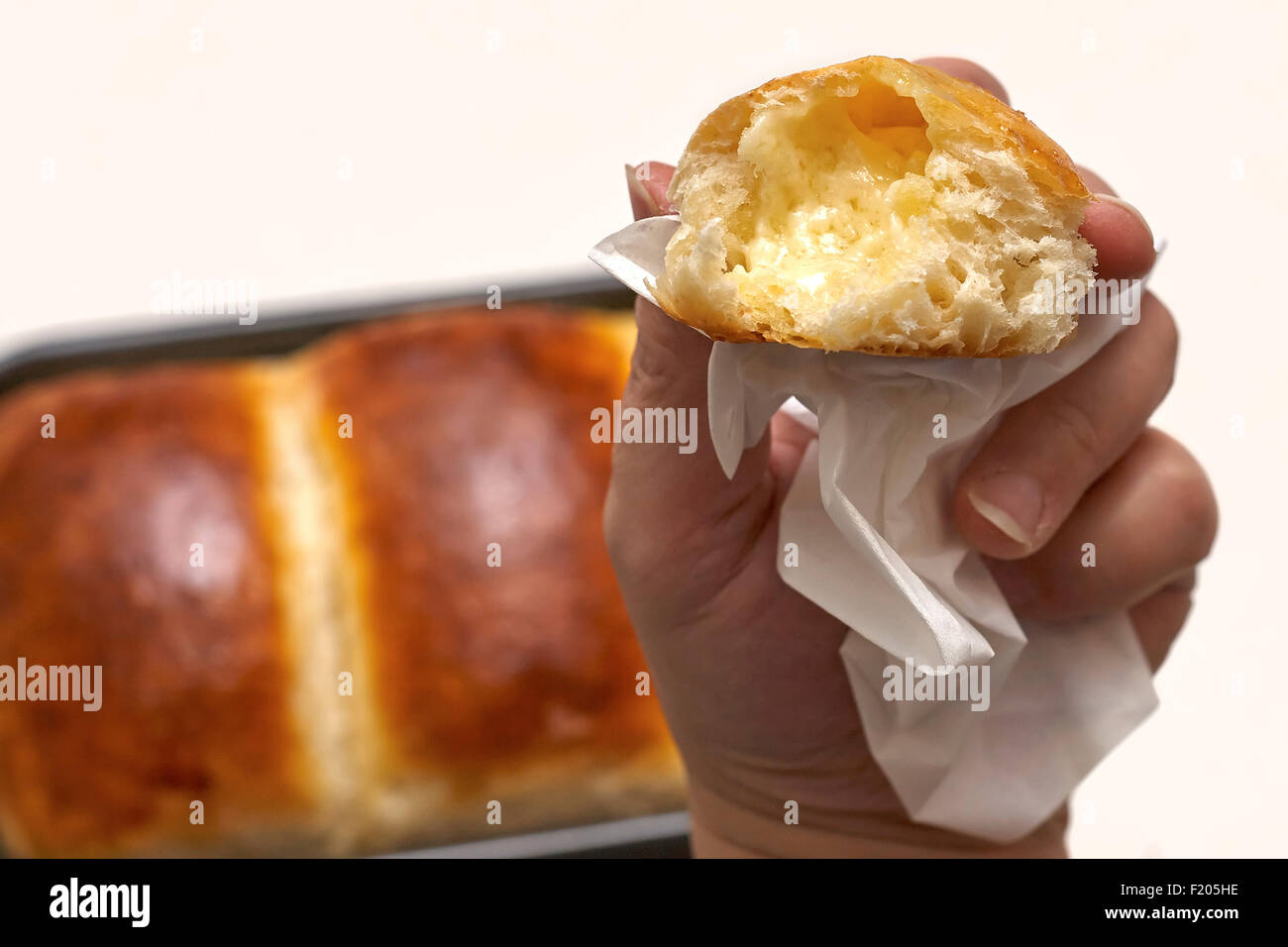 Ladies hand holding up a buttered portion of home baked bread over a baked loaf in the back ground Stock Photo