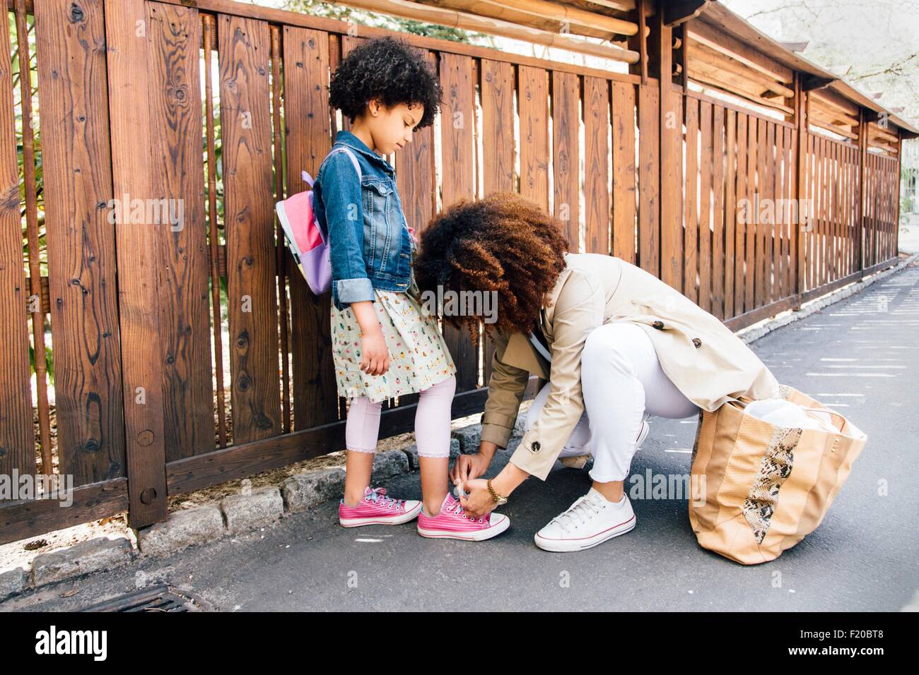 Mother kneeling by fence tying daughters shoelace Stock Photo