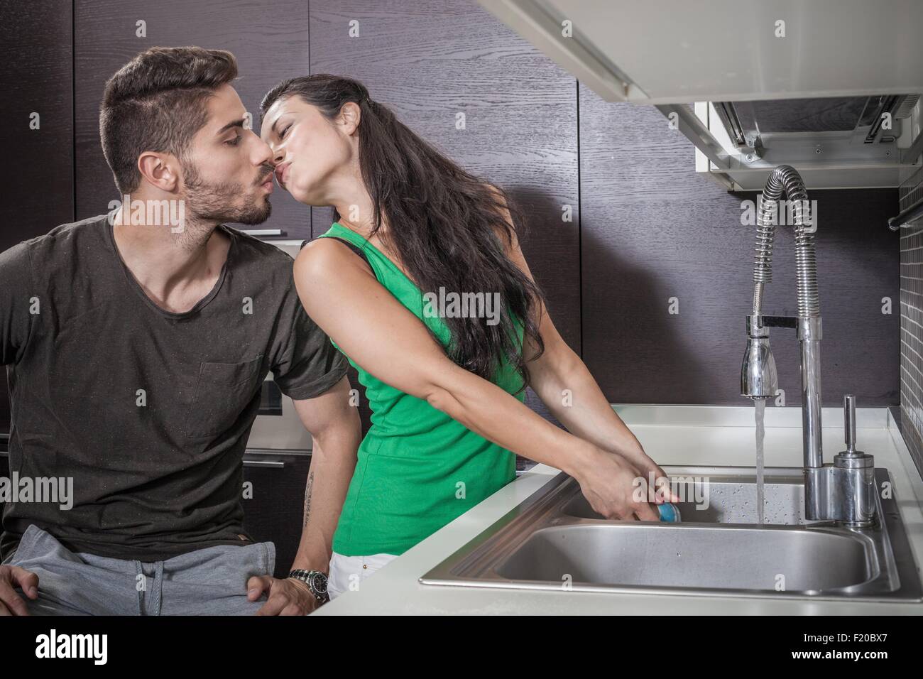 Young woman washing up whilst kissing boyfriend Stock Photo