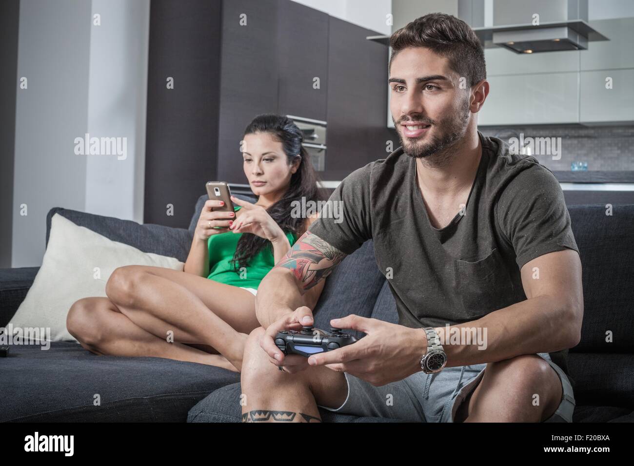 Young couple on sofa using smartphone and gaming control Stock Photo