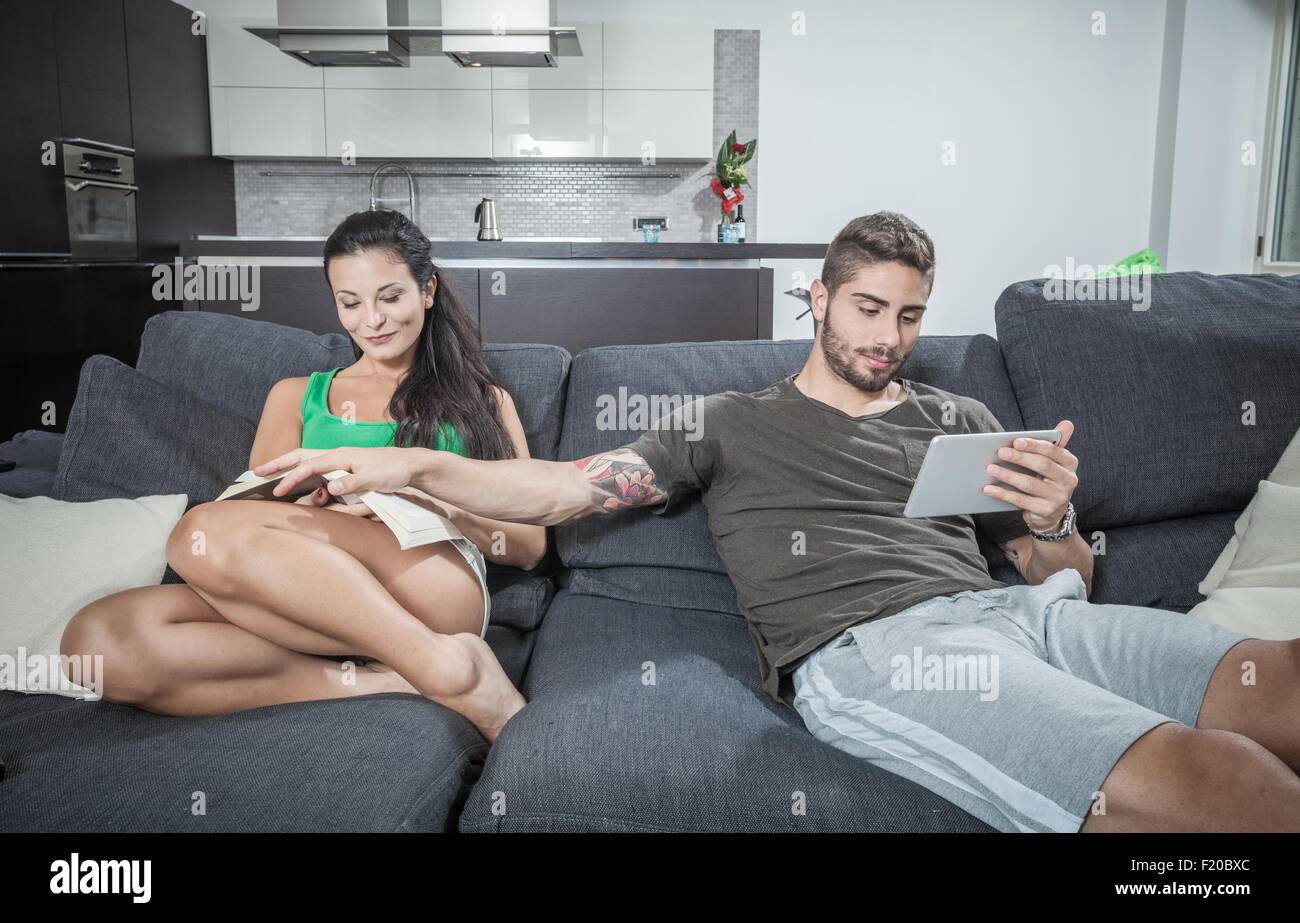 Young man covering girlfriends book on sofa Stock Photo