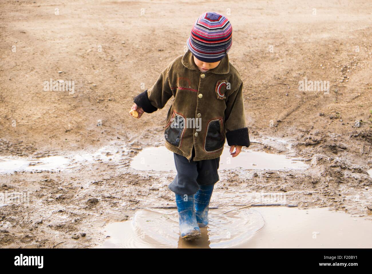 Male toddler wearing rubber boots paddling in puddle Stock Photo