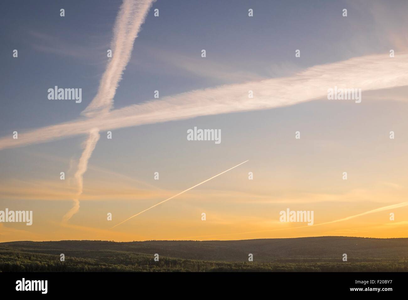 Silhouetted hillside view of sunset sky with criss crossing vapour trails Stock Photo