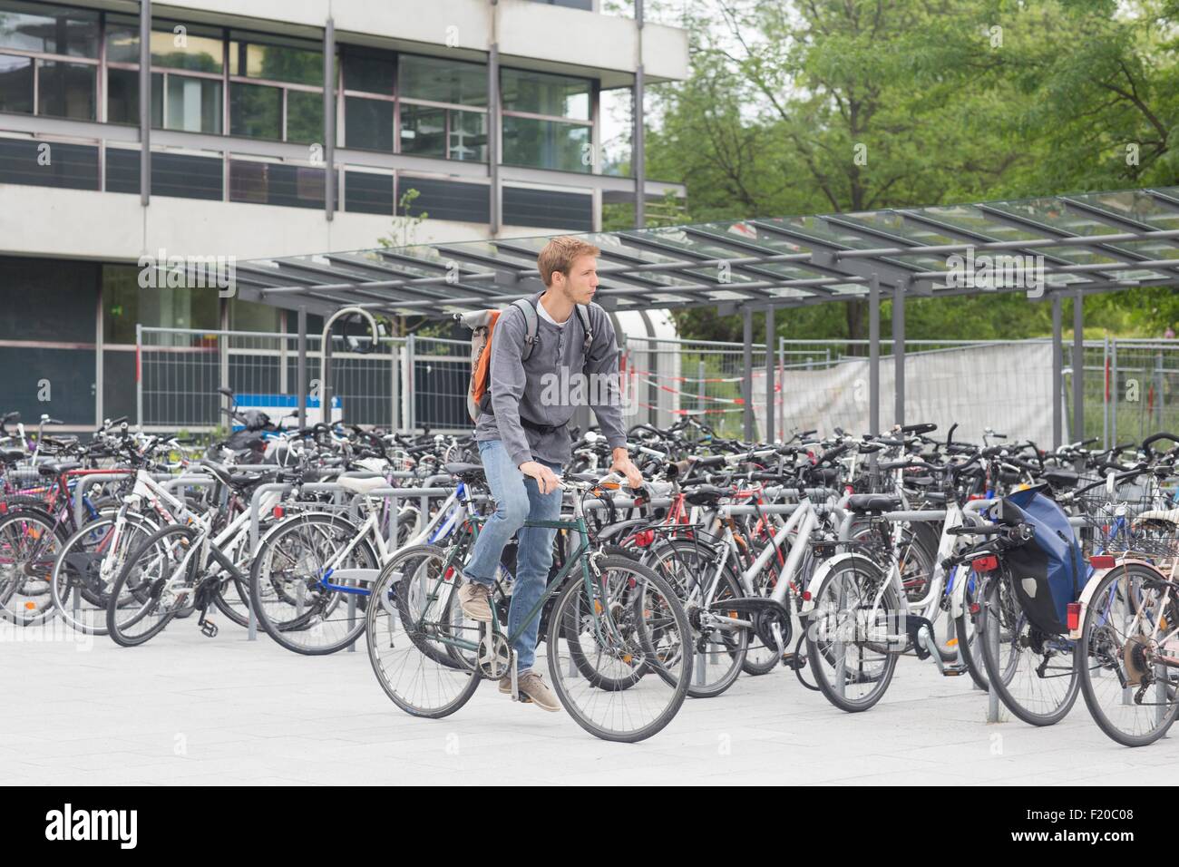 Mid adult man cycling past bike shed full of bicycles, looking away Stock Photo