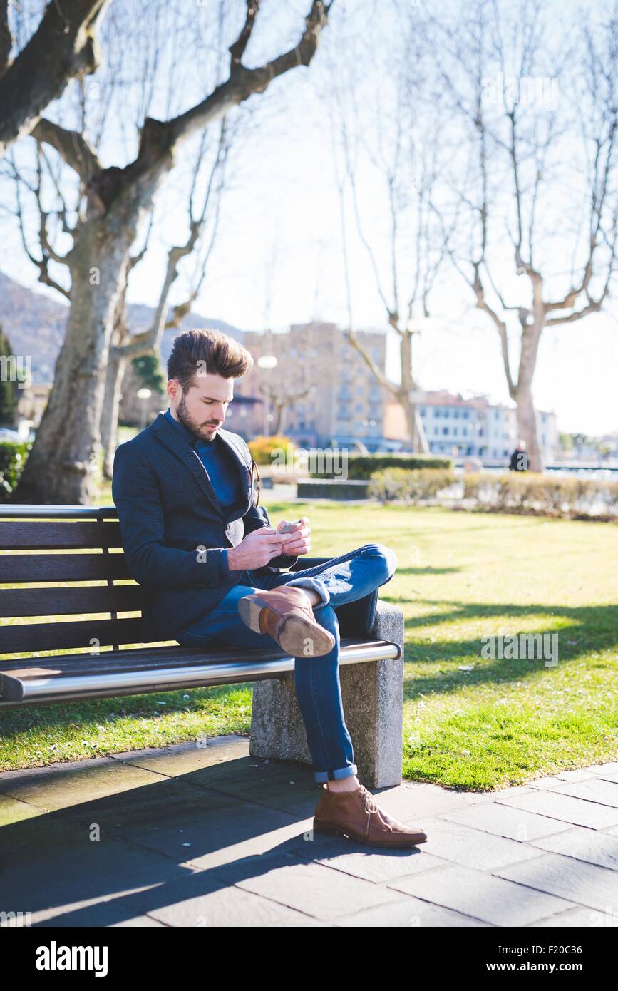 Young man sitting on park bench reading smartphone texts Stock Photo ...